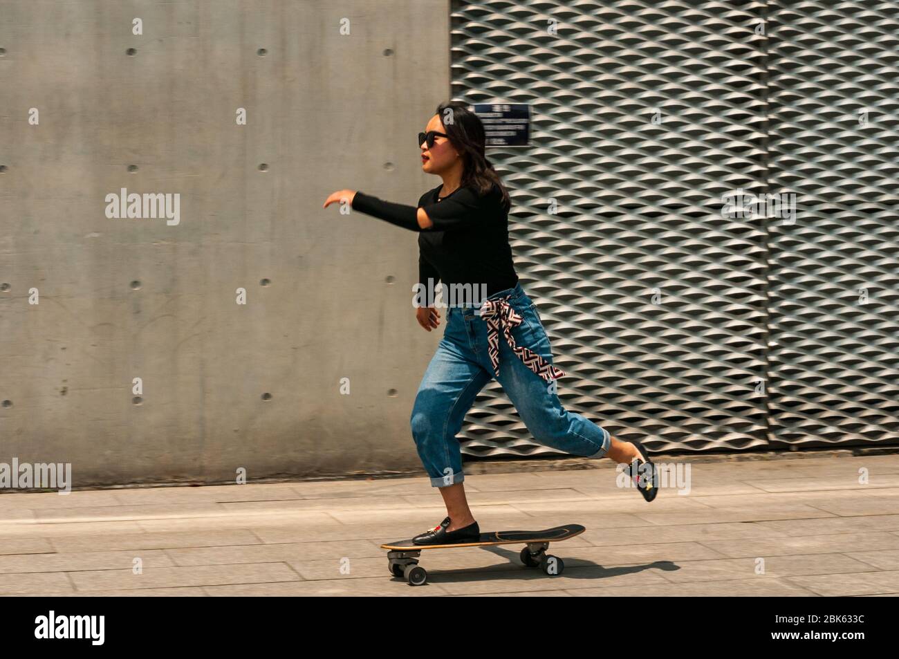 A young Chinese woman skateboarding near the waterfront in front of the