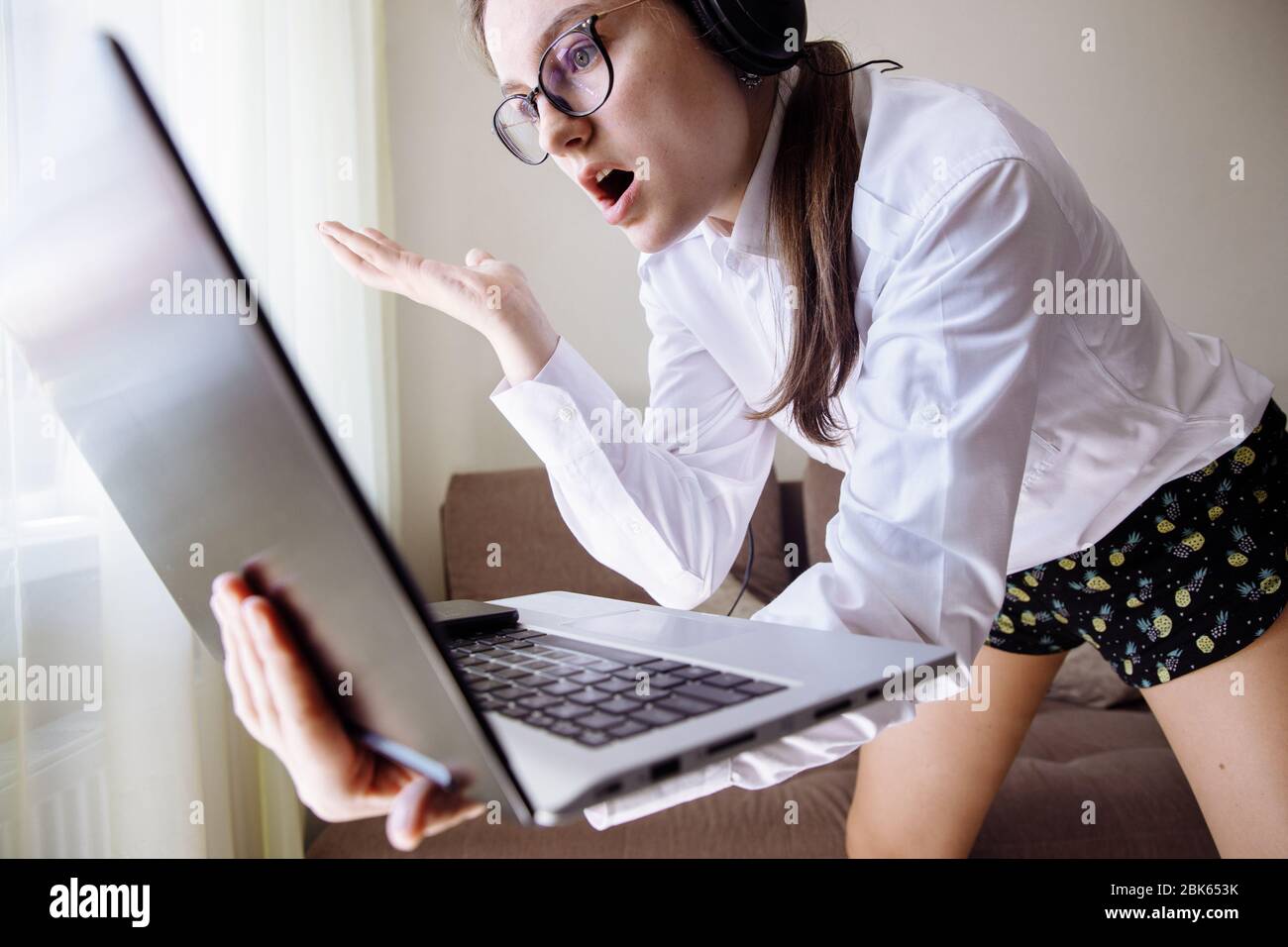 The girl in a home office clothes talking on the web camera. The emotional girl says something and shows her hands.  Stock Photo
