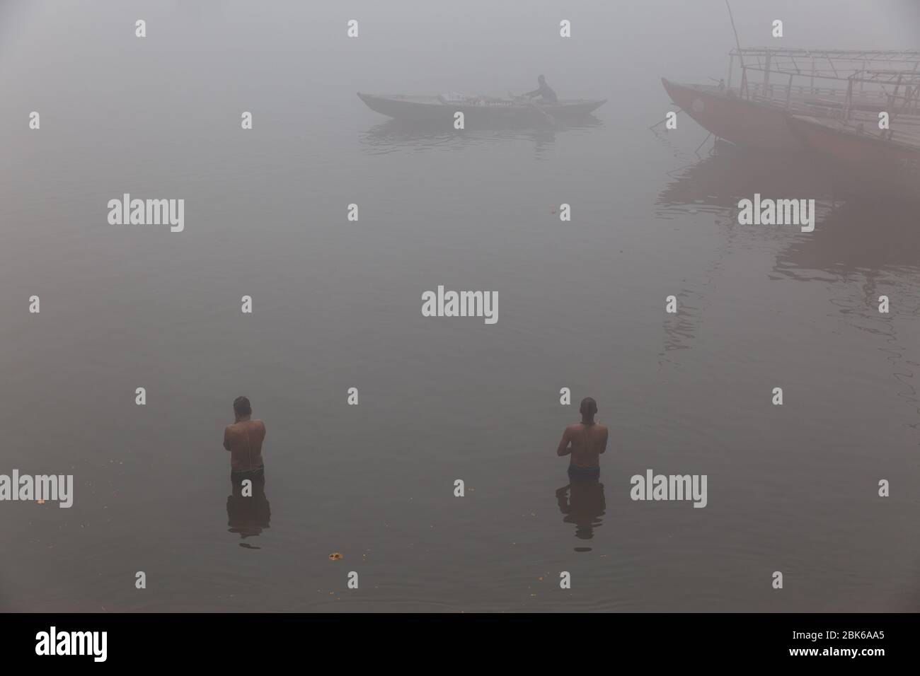 People taking bath on a foggy morning in the river Ganges near Varanasi, India. It's their belief, taking bath in Ganges washing their all sins. Stock Photo