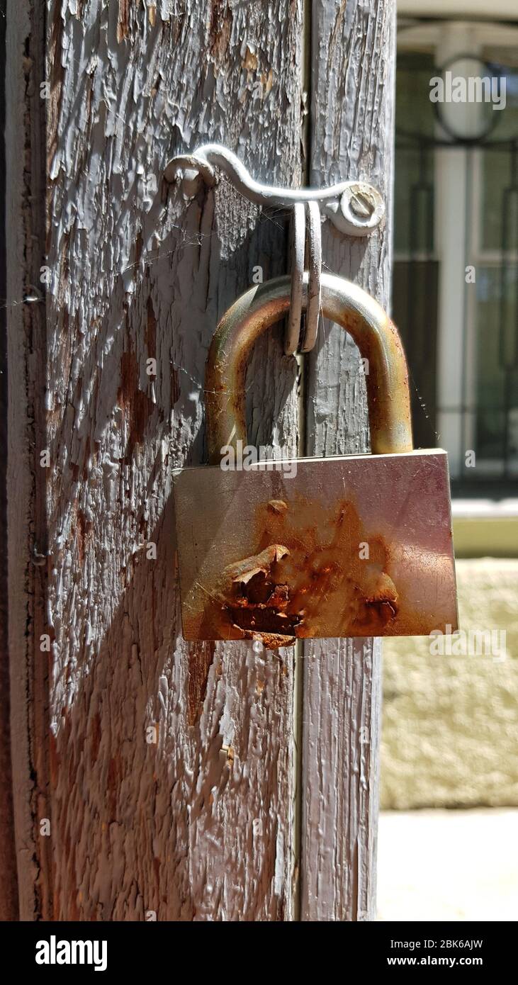 Old rusty padlock with shiny polished metal surface and flaking rust in bright sunlight and shadows. Vintage door lock closeup on blurry rough wooden Stock Photo