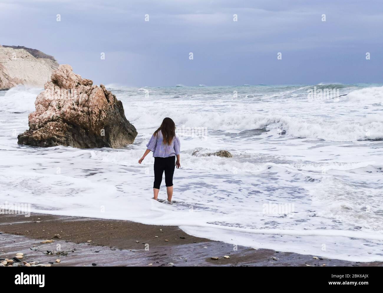 Unrecognized person enjoying the stormy seascape with windy waves. Rock of Aphrodite birthplace, Petra tou romiou coastline at Paphos area in Cyprus Stock Photo