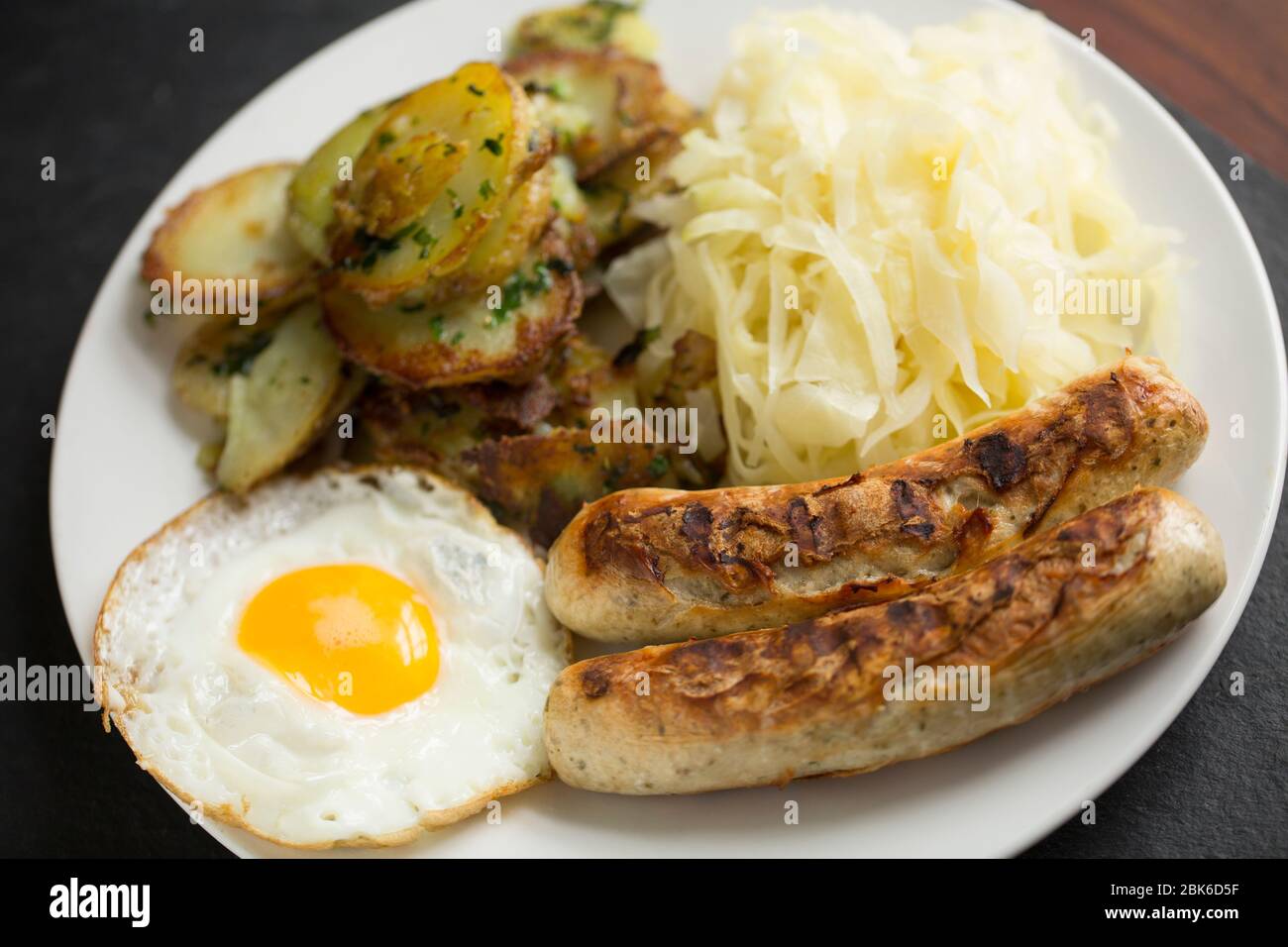 Two grilled Bratwurst sausages served with a fried egg, fried potatoes