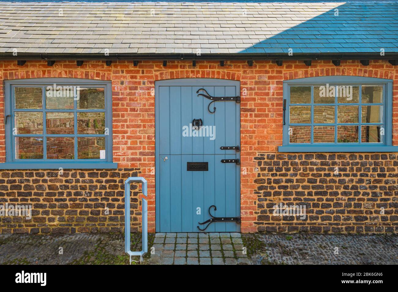 Small brick cottage in village in Southern England during Summer with Blue windows and wooden door Stock Photo