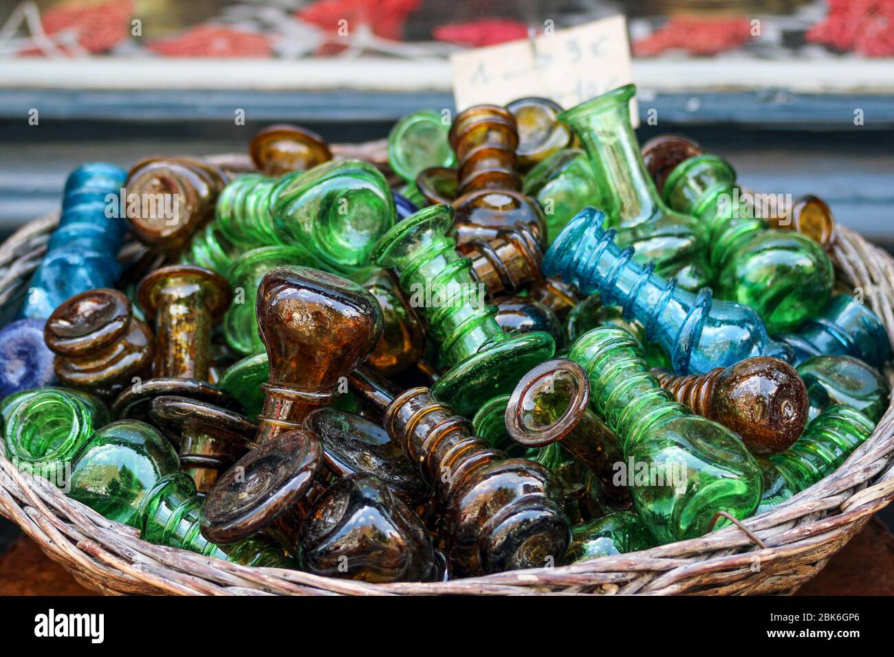 Small green, brown and blue glass bottles or trinkets on sale in a round basket in front of shop Stock Photo