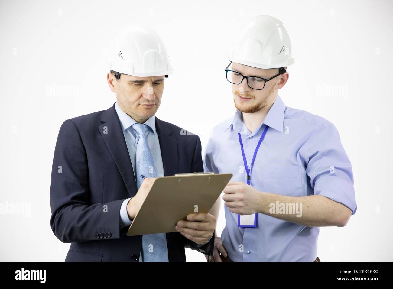 Engineer and architect in hard hats discuss project while making notes in clipboard Stock Photo