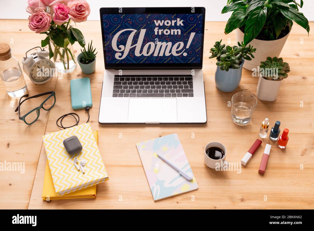 Laptop with notice work from home on display surrounded by flowers, books,  copybook with pen, makeup items, drinks and alarm clock Stock Photo - Alamy