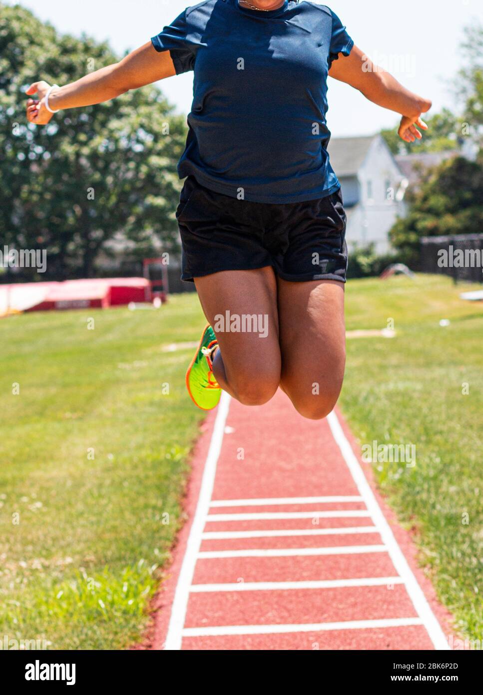 A high school female track and field athlete is practicing the long jump ad flying in the air at the camera. Stock Photo