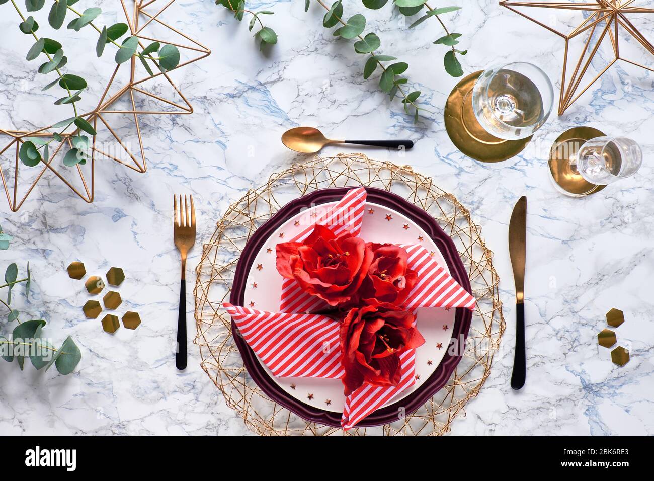 Christmas table setting with red stripy napkin and silk amaryllis flowers. golden utensils and fresh eucalyptus leaves on white marble background. Fla Stock Photo