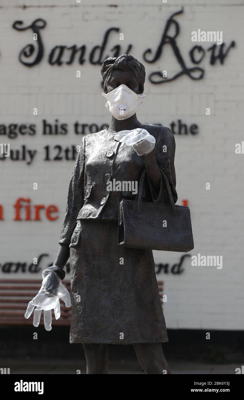 A statue by artist Ross Wilson entitled Mother Daughter Sister, celebrating female identity and culture, in Sandy Row Belfast is adorned with a mask and disposable gloves as the UK heads towards a seventh week in lockdown to try and limit the spread of coronavirus. Stock Photo
