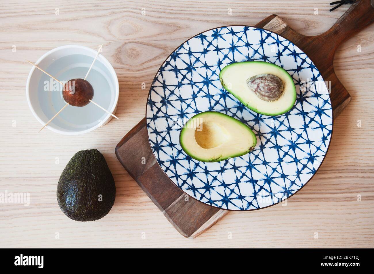 Top view of avocado fruit on ceramic vintage dish and seed inside pot for growing a plant. Avocado seed in water for reproduction of seedlings. Health Stock Photo