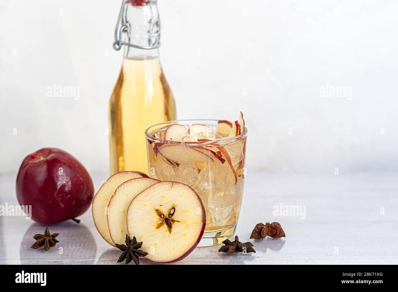 Healthy organic foods. Apple cider in a glass bowl and fresh red apples on a light background. In a glass of ice cubes and nearby cinnamon sticks. Cop Stock Photo