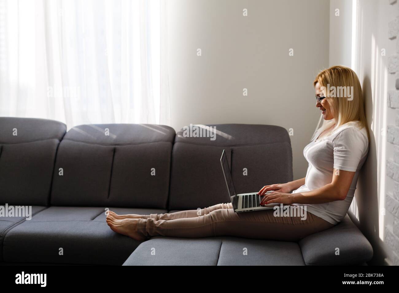 Woman using a laptop while relaxing on the couch Stock Photo - Alamy