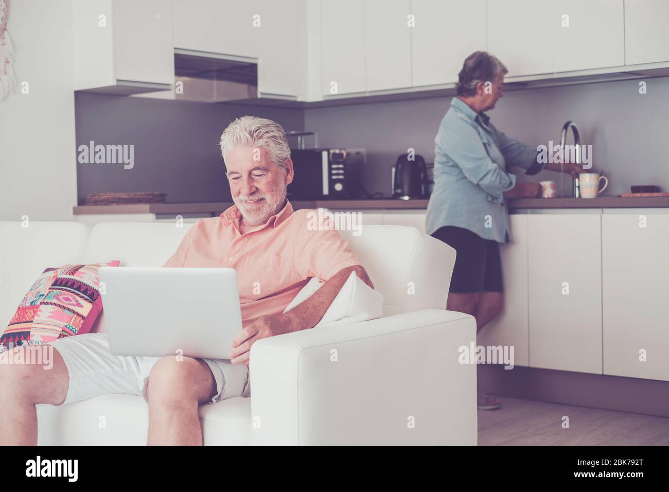 Stayhome and lockdown coronavirus old people concept - senior caucasian couple inside house in the kitchen cooking and use modern connected laptop com Stock Photo