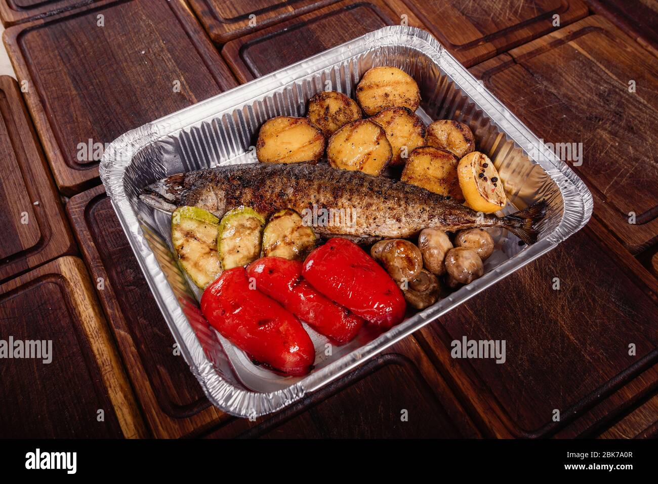Appetizing mackerel fish baked on fire with spices, served on a plate and decorated with vegetables on wooden background Stock Photo