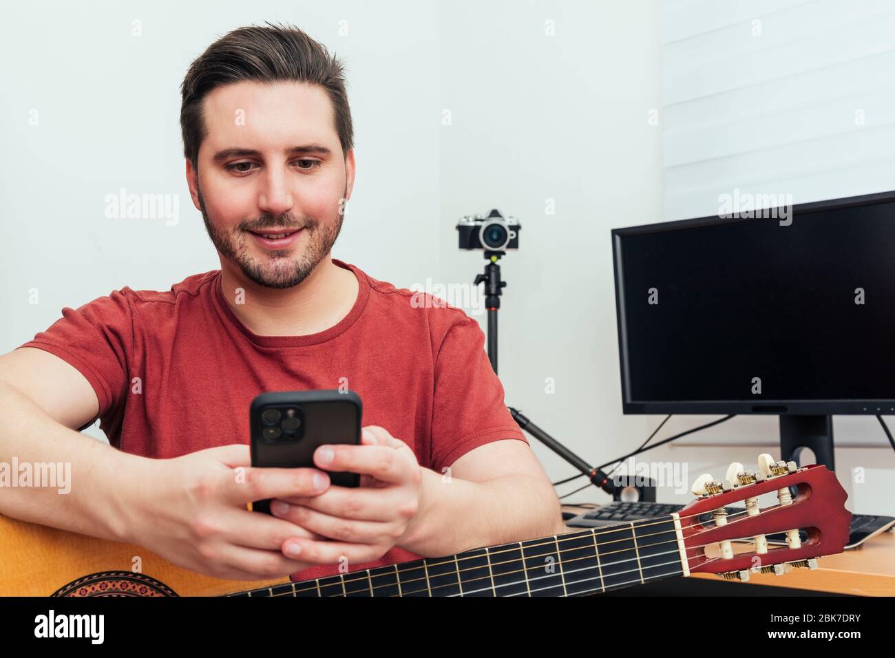 Blogger checking his phone before giving the guitar lesson from his home recording studio. Learning online concept. Stock Photo