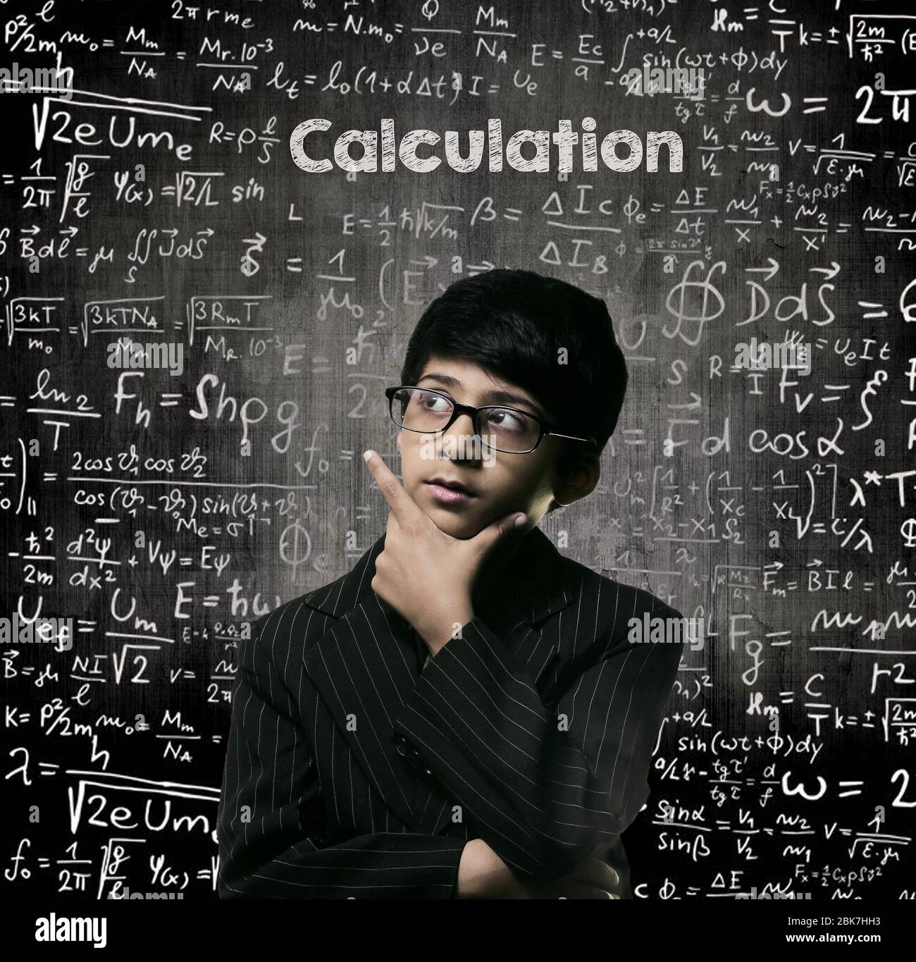 Cute Intelligent Little Boy Looking Up Thinking andWearing Glasses Standing Before A Chalkboard, Chemical Formulas Are Written On Board With The Chalk Stock Photo