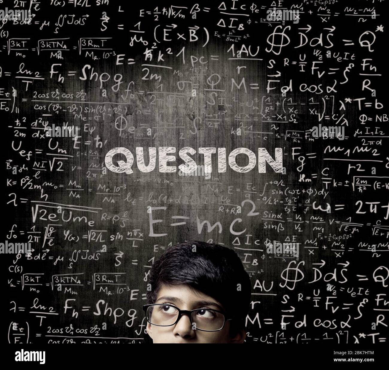Cute Intelligent Little Boy Looking Up Thinking andWearing Glasses Standing Before A Chalkboard, Chemical Formulas Are Written On Board With The Chalk Stock Photo
