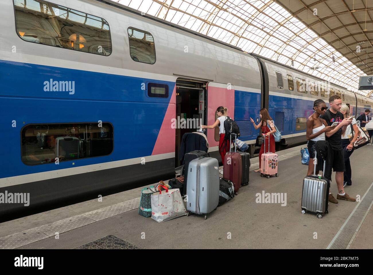 Passengers boarding a double decker train with many pieces of luggage