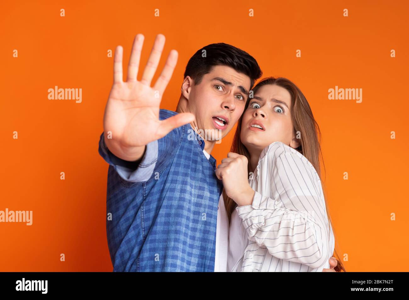 Guy protects frightened girl on orange background Stock Photo