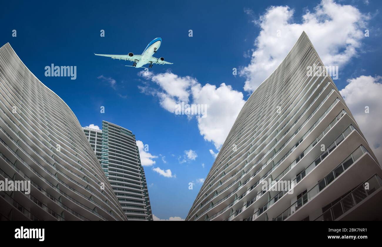 Commercial airplane flying over tall skyscrapers in the city. Bottom view. Stock Photo