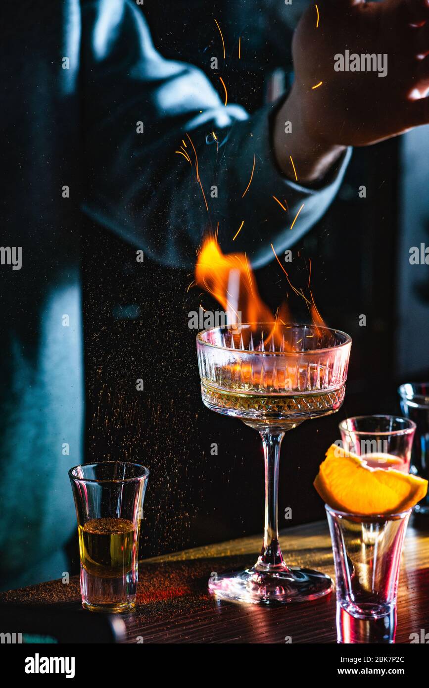 Male bartender holds fired up sugar above delicious alcohol cocktail Stock Photo