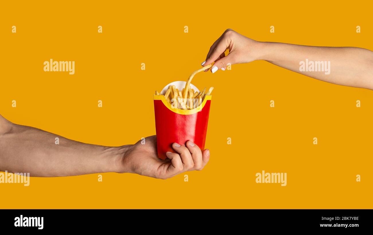 KHARKIV, UKRAINE - APRIL 4, 2020: Closeup of guy and girl eating french fries from McDonald's, orange background Stock Photo