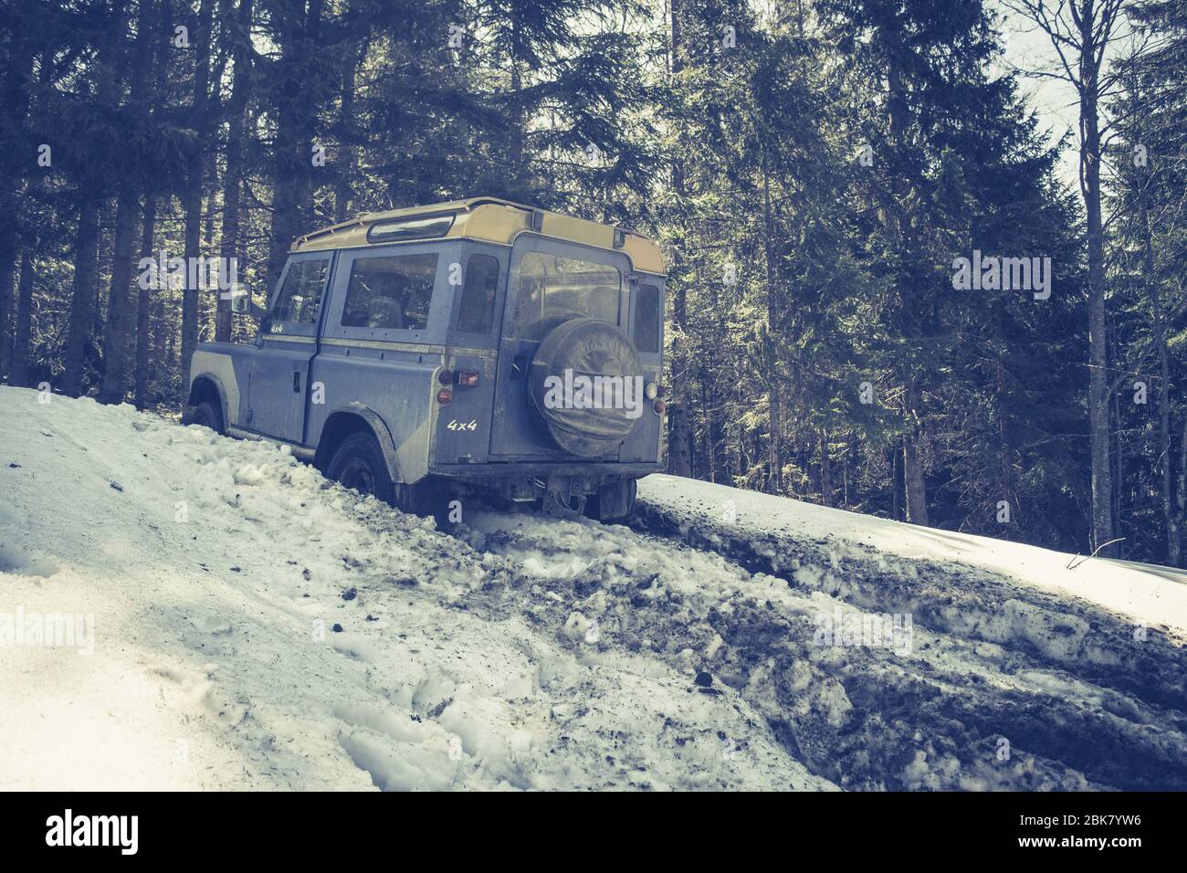 Blue SUV Sticks in Deep Snow Slips. Jeep Driving Along a Forest Road and Stuck in Pile of Mud and Snow. Stock Photo