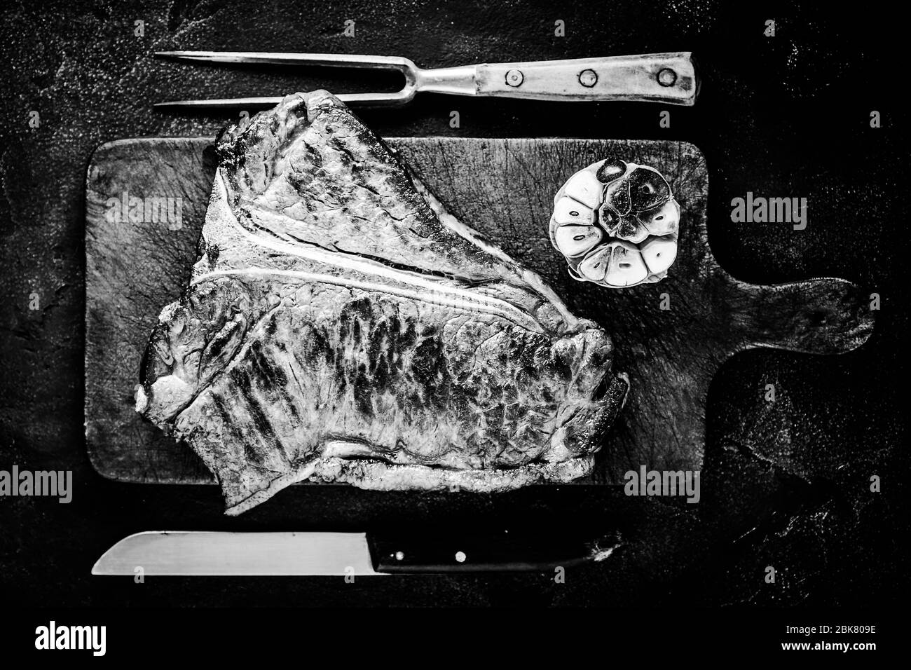 Grilled Dry Aged Premium T-bone Steak on Dark Rustic Chopping Board. Black and White USDA Prime Beef. Stock Photo