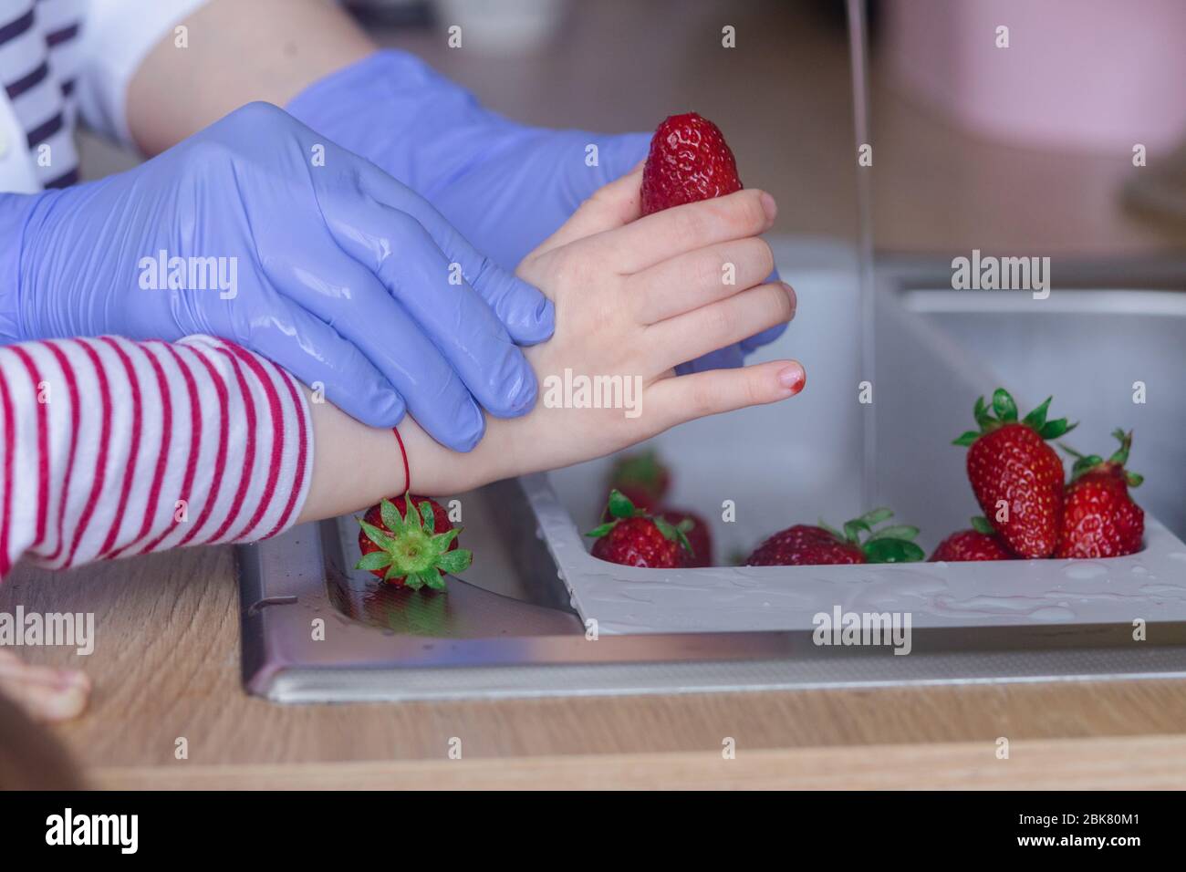 Children and adults wash their strawberries in the kitchen sink Stock Photo