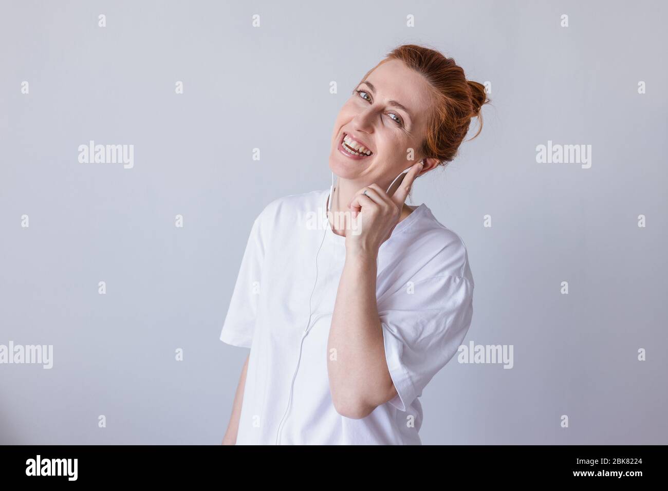 Nice young girl redhead with headphones laughing looking at camera over white background. Stock Photo