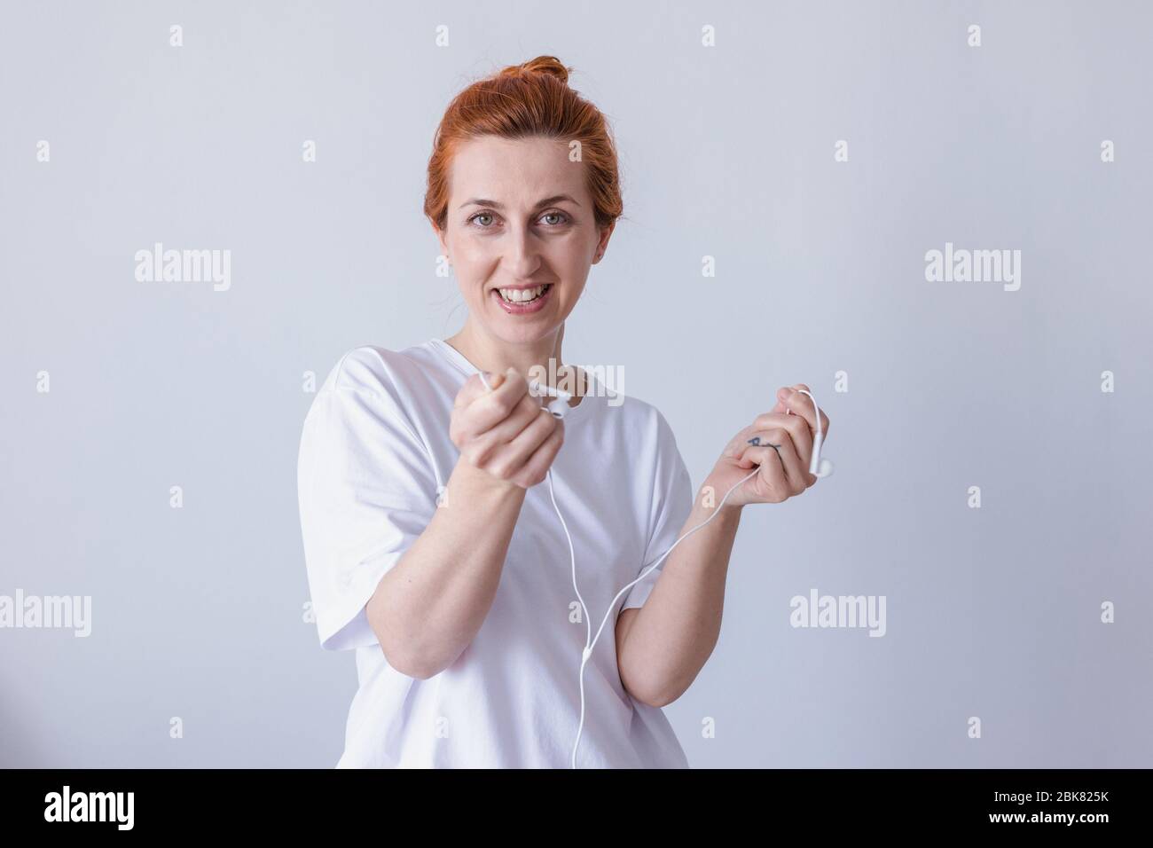 Nice young girl redhead with headphones laughing looking at camera over white background. Stock Photo