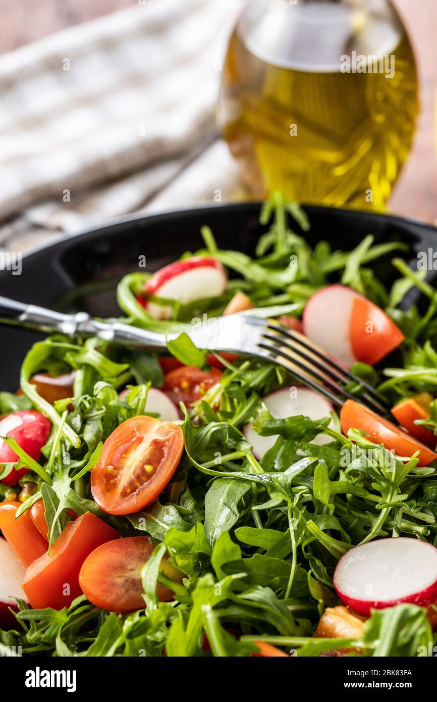 Fresh arugula salad with radishes, tomatoes and red peppers on plate. Stock Photo
