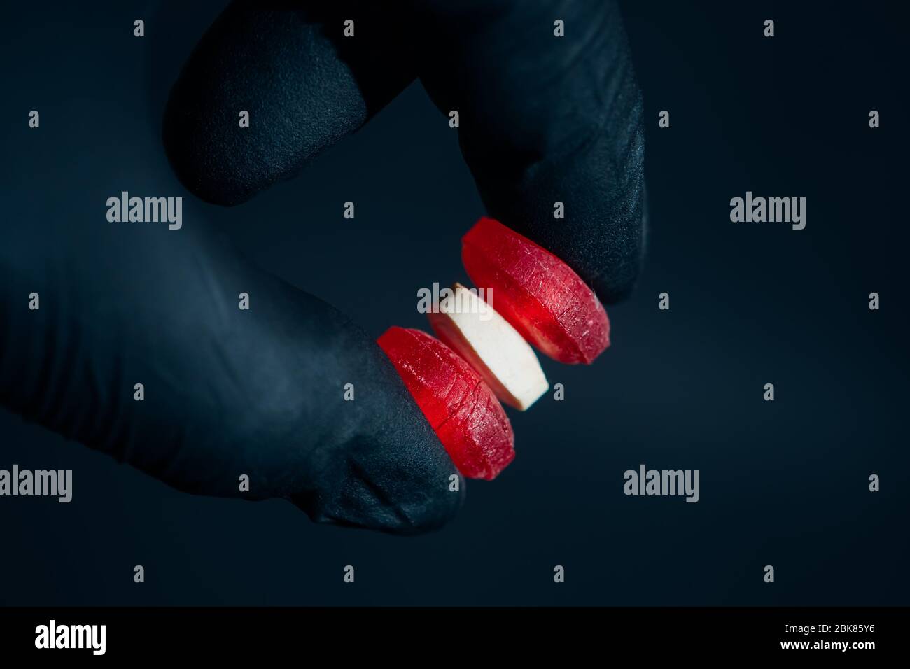 Holding yellow pills in hand with gloves close up on dark background Stock Photo