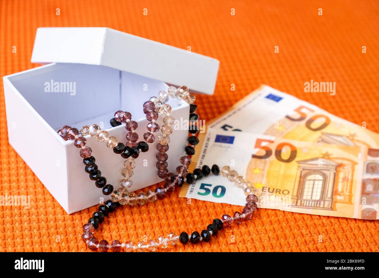 Beautiful Female Beads in White Gift Box and Paper Banknotes Euro Lay on a Orange Fabric Textured Background. Stock Photo