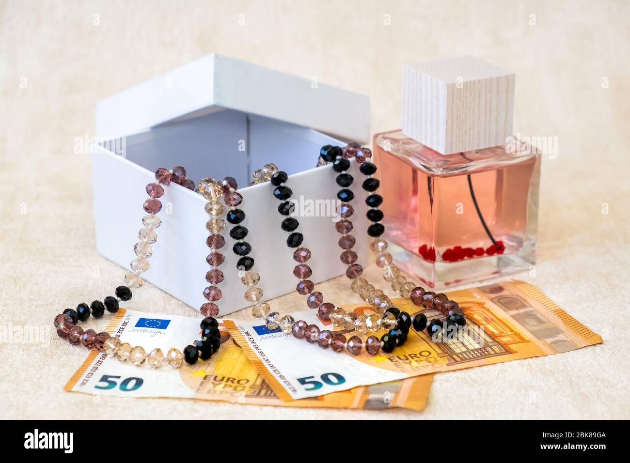 Beautiful Female Beads in White Gift Box, Perfume,  and Paper Banknotes Euro Lay on a White Textured Background. Stock Photo