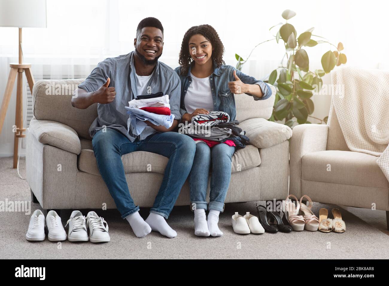 Young Black Couple Sitting Beside Folded Clothes And Shoes At Home Stock Photo