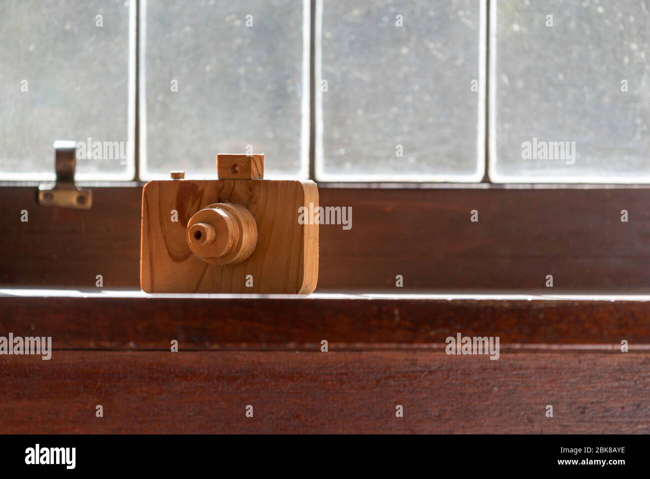 A hand made model of a wooden camera sits in the warm sun on a timber window ledge in front of a lead light window Stock Photo