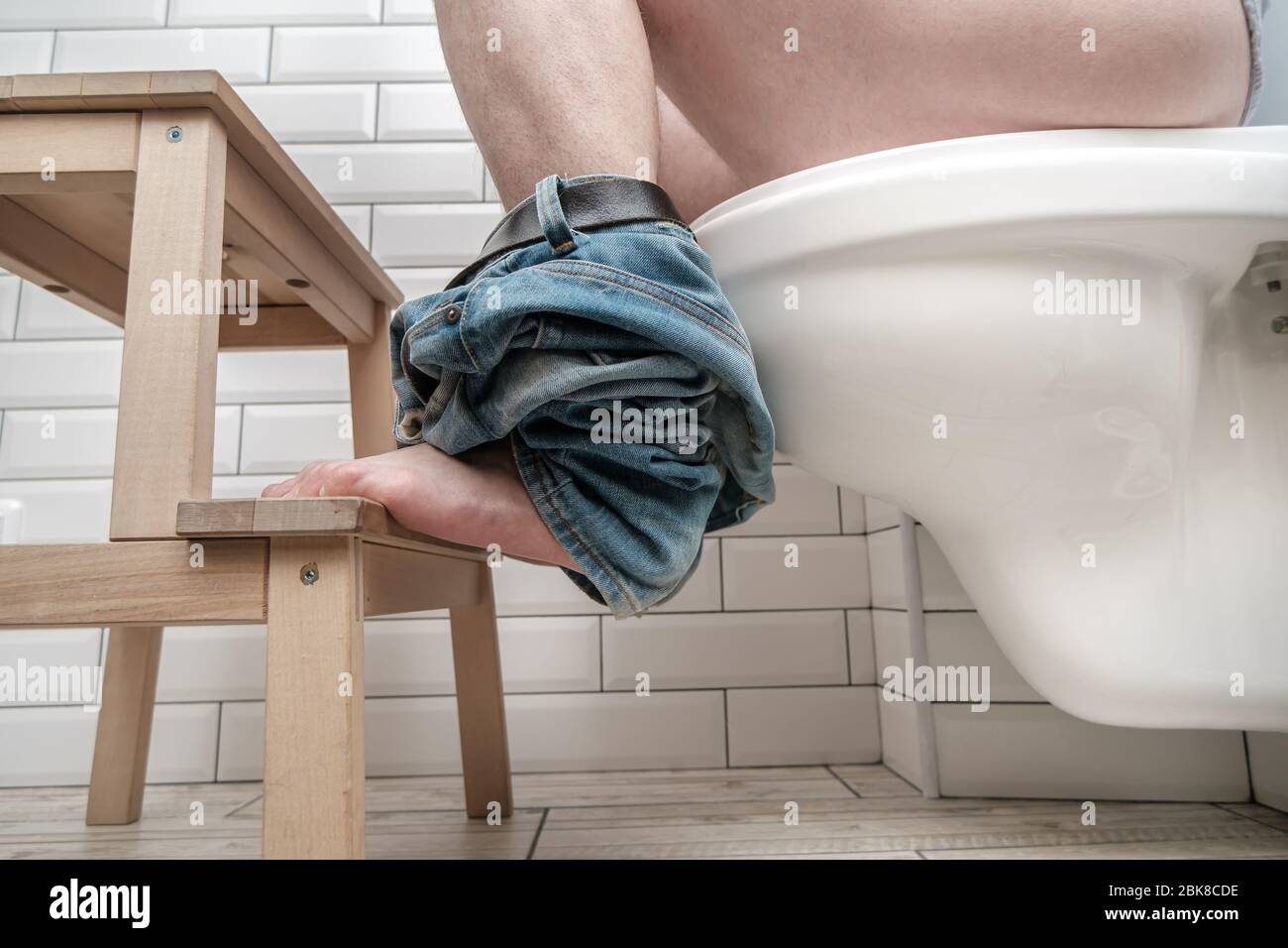 Man sitting on toilet bowl properly, he put feet on a small stool in a squatting position, during the defecation. Health concept. Stock Photo