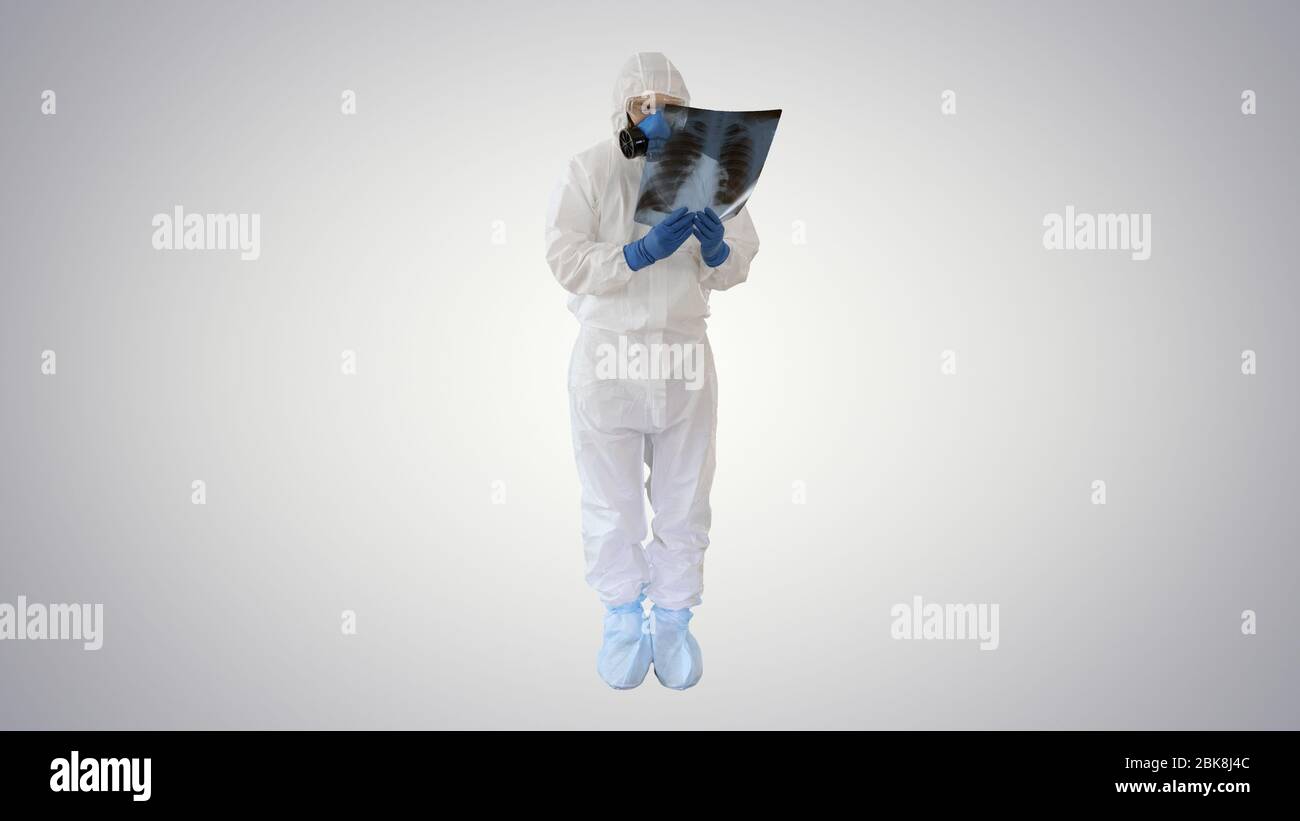 Infectious disease doctor in protective antibacterial suit and medical mask Pulmonologist examines an x-ray of lungs on gradient background. Stock Photo