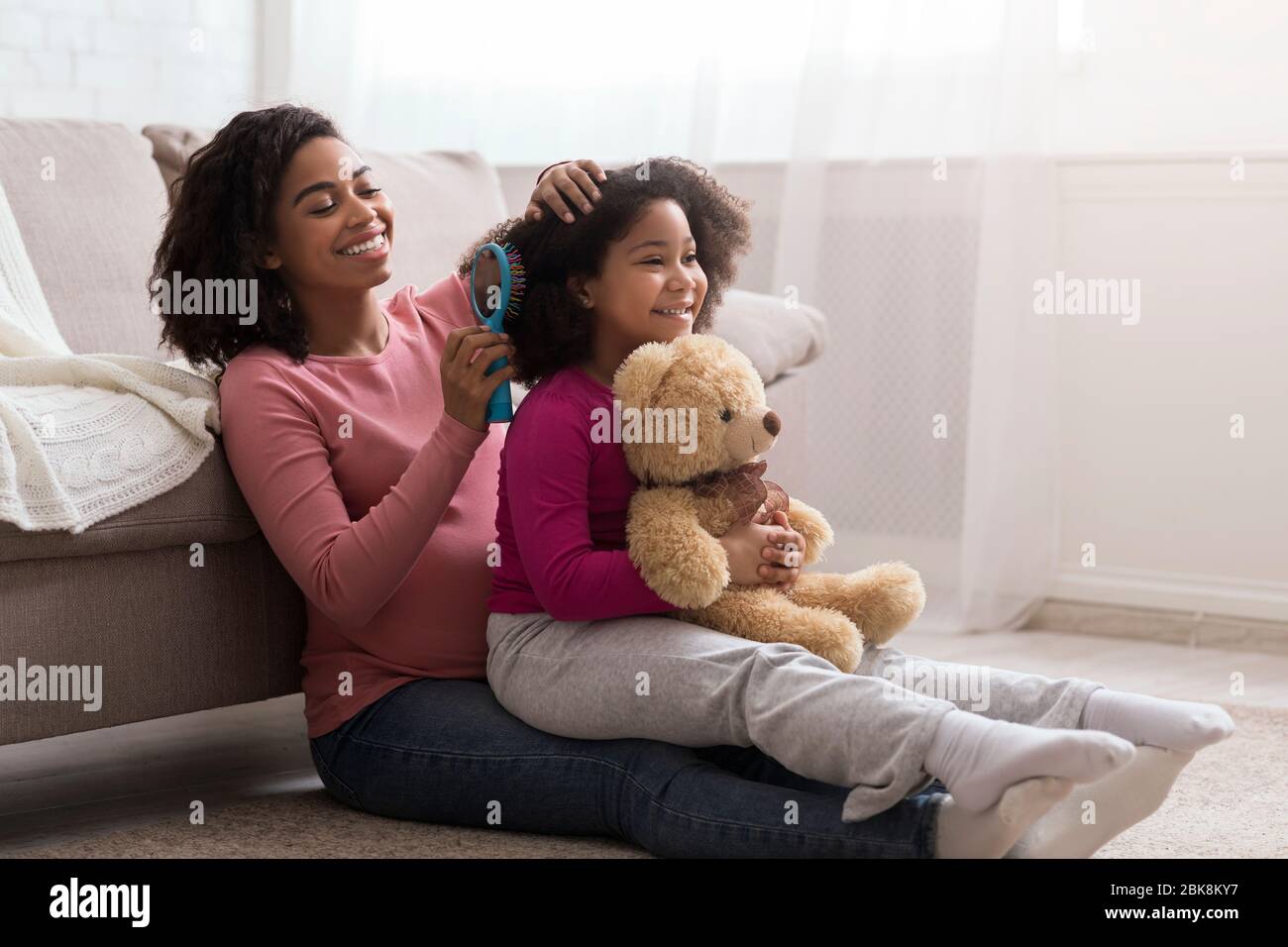Caring pregnant african mom combing her little daughter's hair at home Stock Photo
