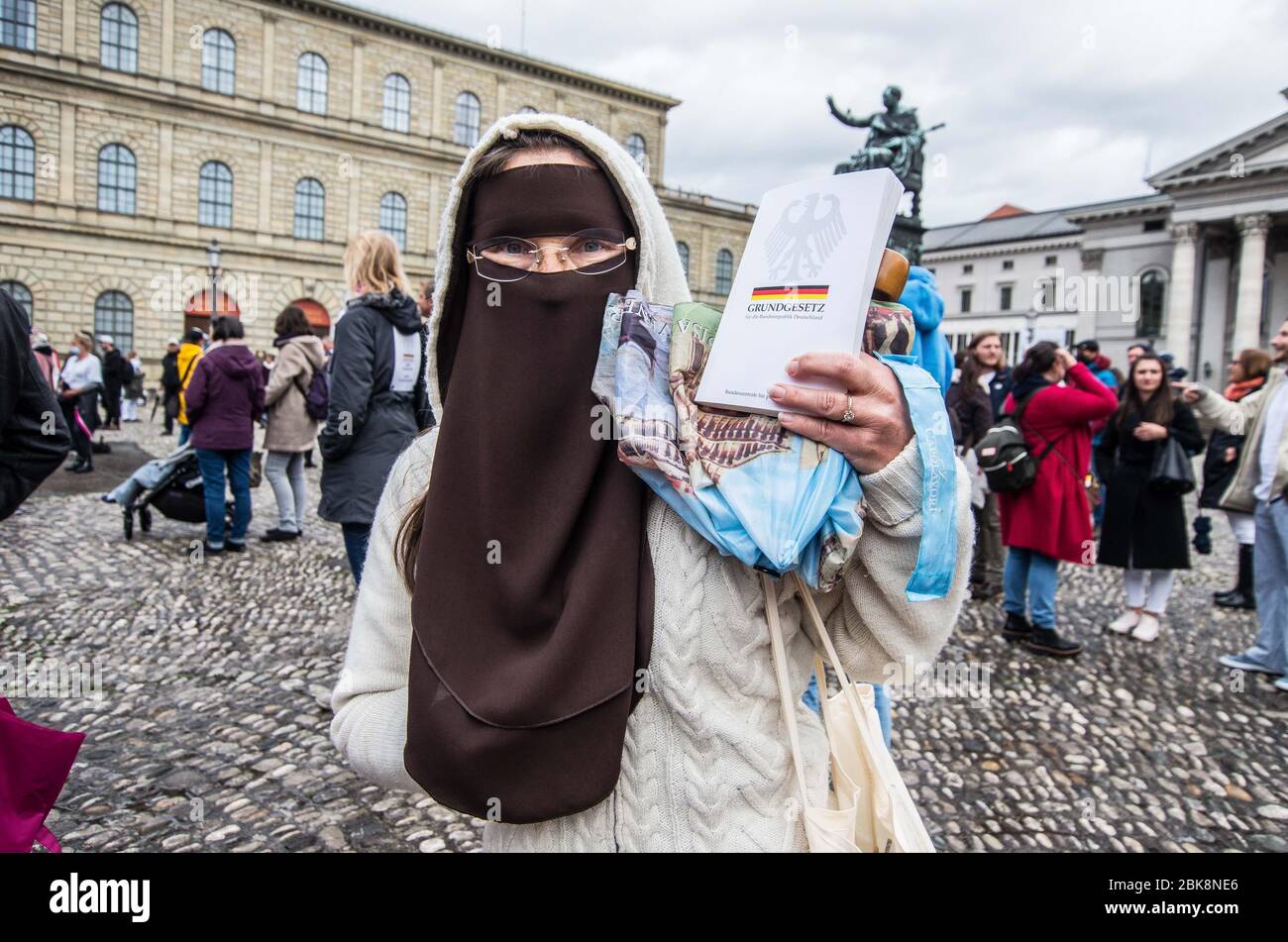 Munich, Bavaria, Germany. 2nd May, 2020. A woman wearing a niqab as a provocation holds the German Grundgesetz up at a conspiracy demo in Munich, Germany. On the heels of a violent attack against ZDF journalists in Berlin, the Munich Hygienedemos took place again, complete with conspiracy theorists, right-extremists, neonazis, Hooligans, AfD members, insults and aggression towards journalists and police, and violations of the infection protection laws. Organized in Telegram chats by conspiratorial 'Querfront'' (cross-front) groups, the organizers planned several individual demos with instru Stock Photo