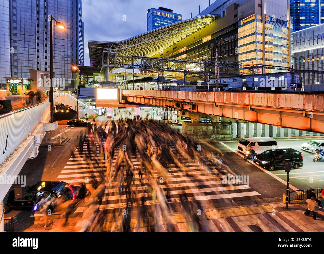 Crowded street crossing in Osaka city near OSaka umeda railway train station at sunset. Stock Photo