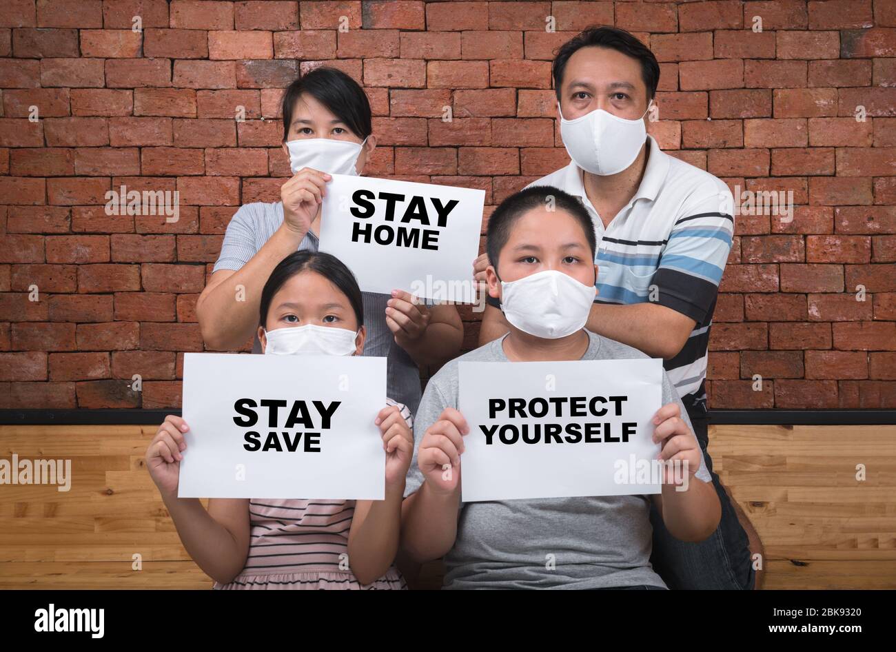 Asian  Family wear mask and shows paper with stay home stay save words at home, Coronavirus, COVID-19, self-quarantine, social disdancing concept. Stock Photo