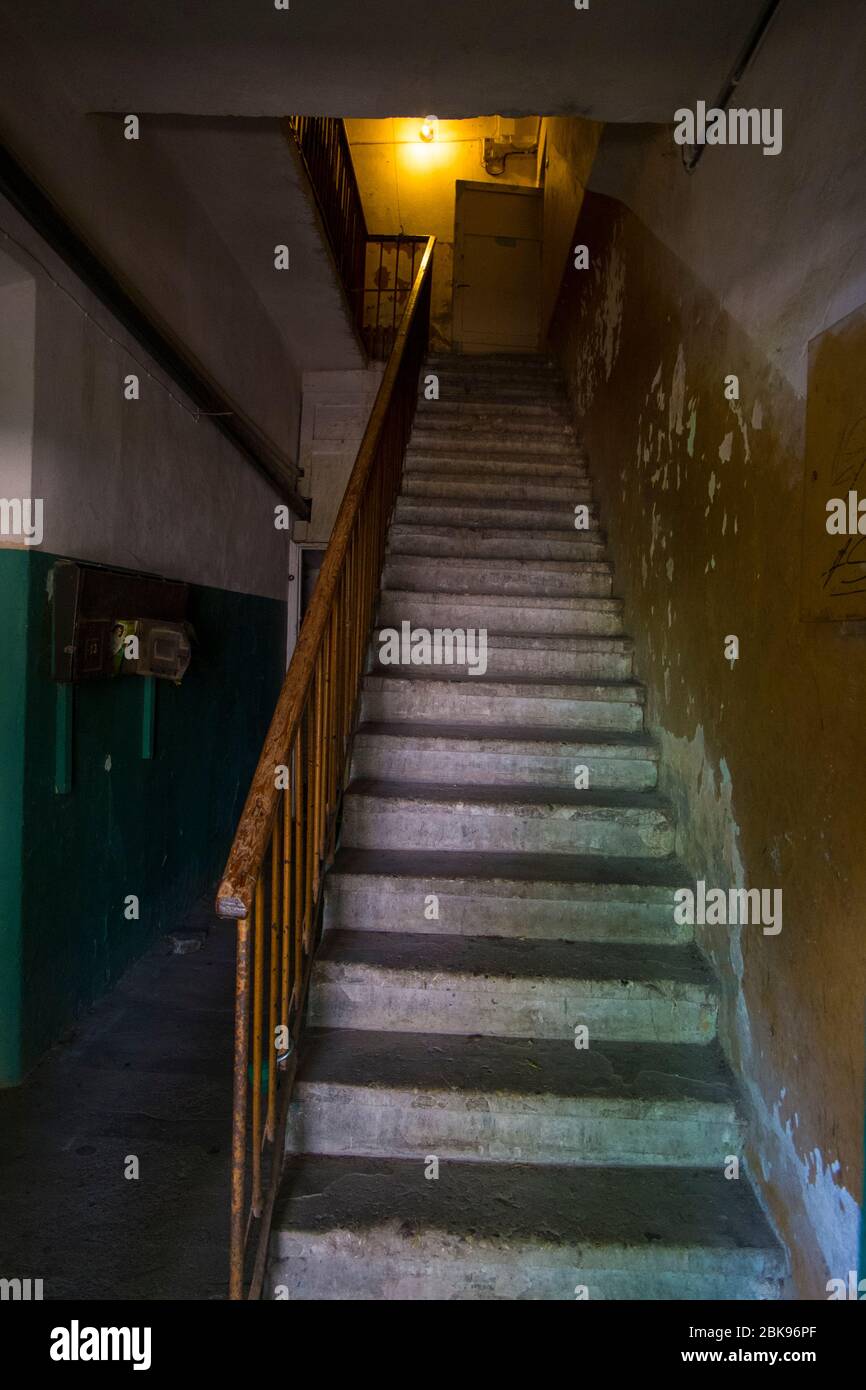 A bent, dark, scary, stone, worn staircase in a USSR, Communist era apartment building. In Vilnius, Lithuania. Stock Photo