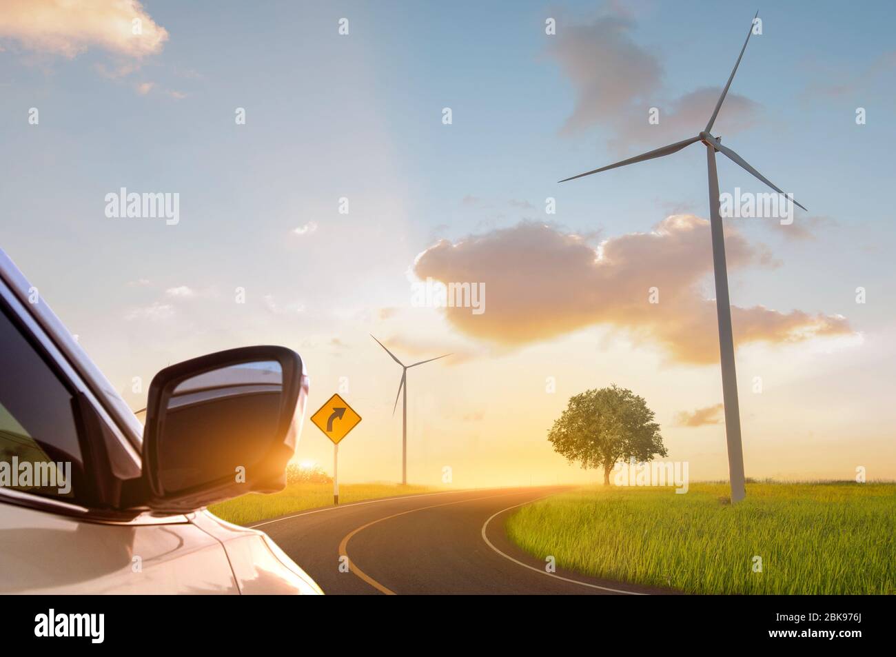 Green energy concept. Road in green field with wind turbines and sunset backgrounds. Stock Photo