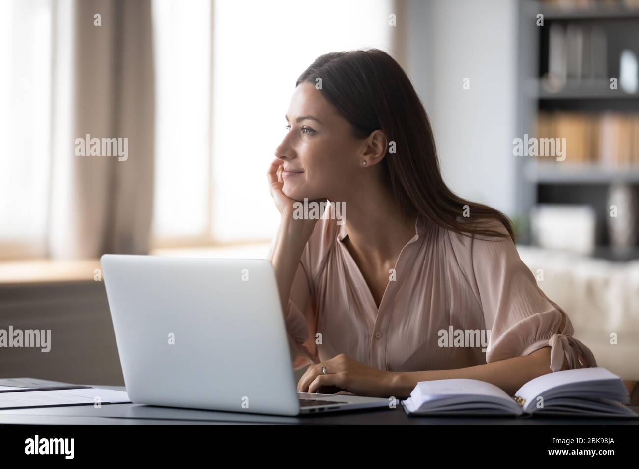 Dreamy young woman pondering ideas, sitting at desk with laptop Stock Photo