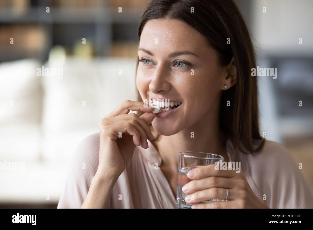 Close up smiling woman taking pill, holding water glass Stock Photo
