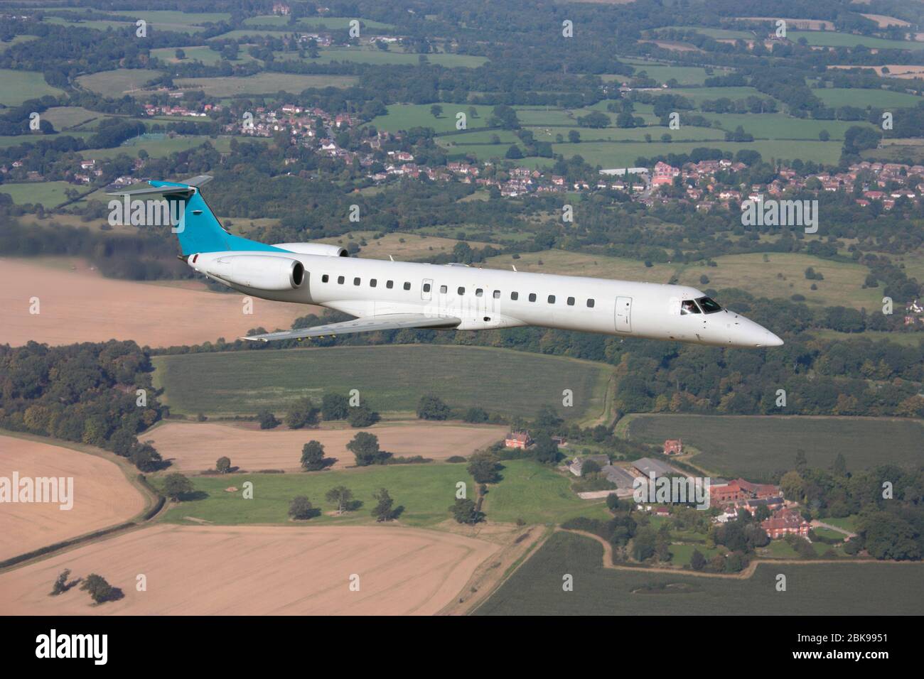 Small regional passenger jet plane flying over countryside on a short haul flight. Air travel, civil aviation and flights. Aerial view. Stock Photo