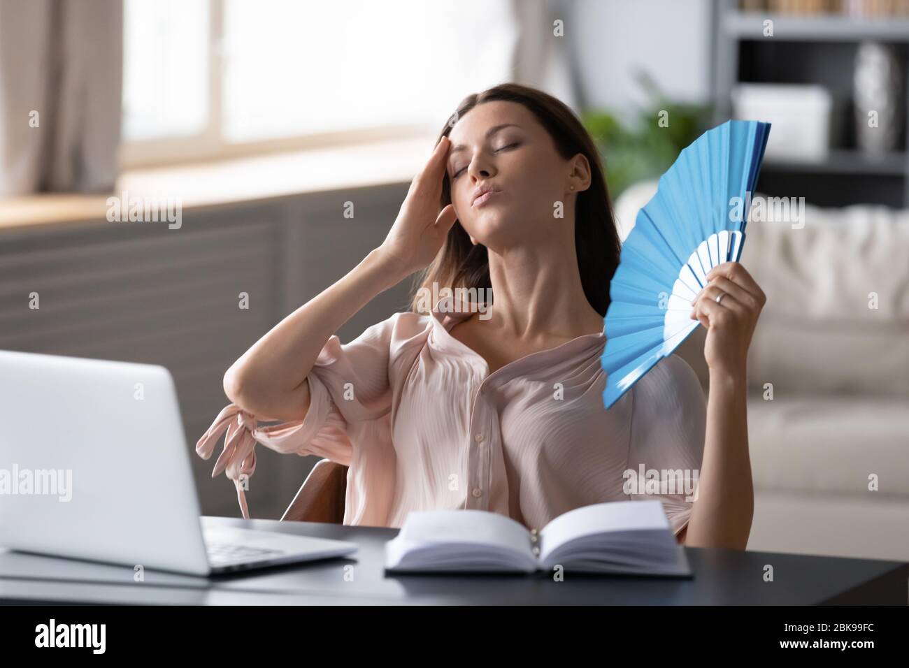 Overheated woman waving fan, touching forehead, suffering from heating Stock Photo
