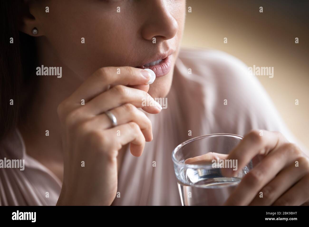 Close up young woman taking pill, holding water glass Stock Photo